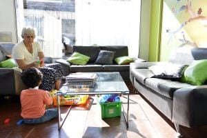 Una abuelita y su nieto jugando dentro de la Sala Familiar Ronald McDonald en Sotero del Rio. Hay varios sofás negros con cojines verdes y naranjados.