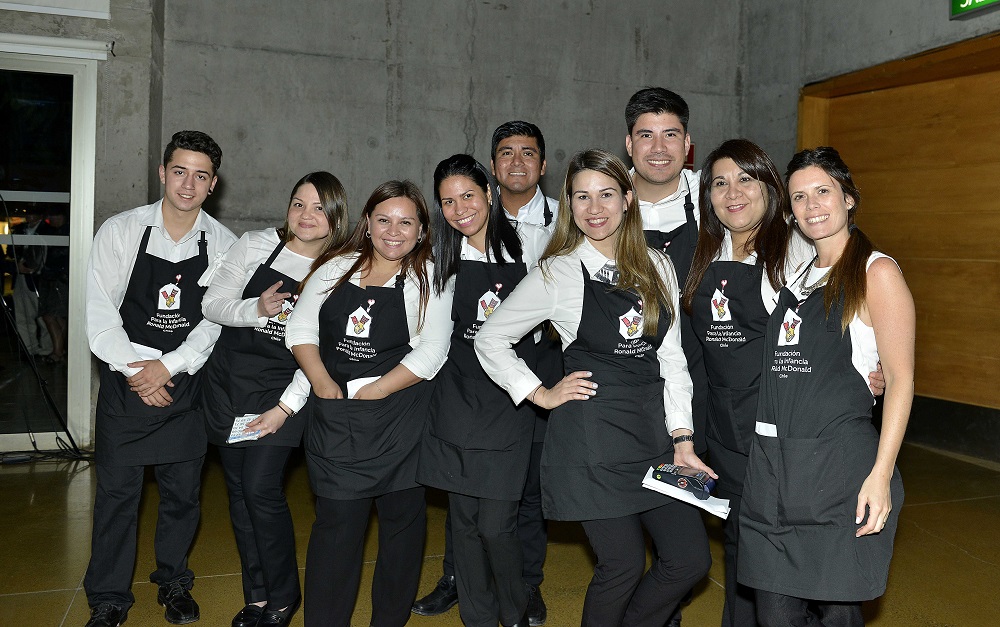 Grupo de hombres y mujeres usando delantales marcados con el logo de la fundación. Sonríen al hacer parte de la Cene de Gala.
