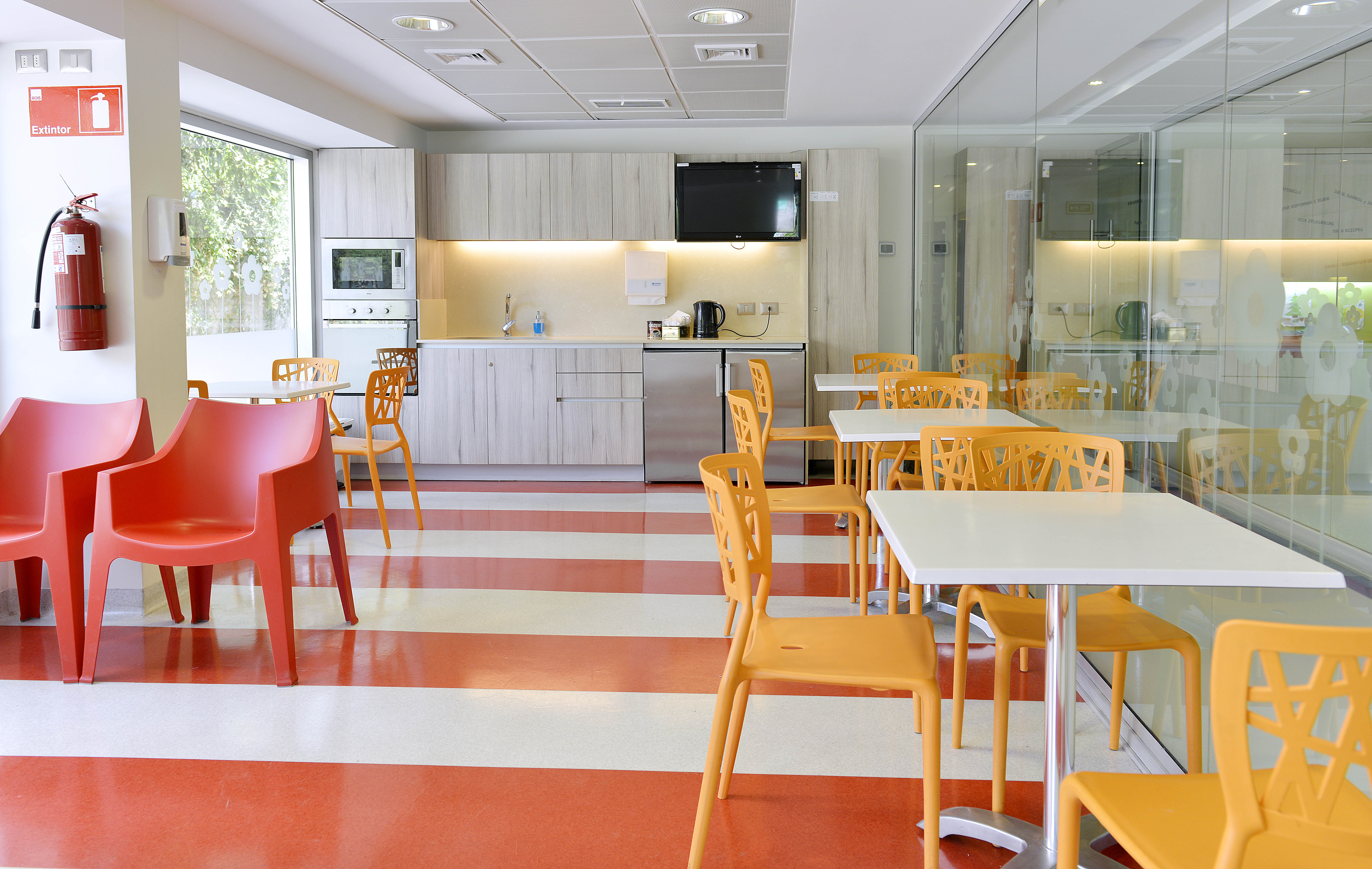 Interior de la Sala Familiar Ronald McDonald en Troi. Los pisos de rayas rojas y blancas. Se ven mesas blancas y sillas rojas y amarillas; también una cocina.